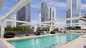 Zona de piscina en la azotea con sillones y sombrillas, rodeada de edificios altos.