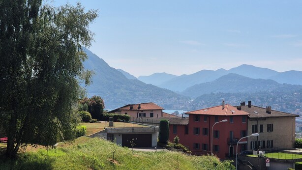 A hillside residential area with houses, a street, and mountains in the background. - Executive Huge Flat in Central Lugano (Lugano)