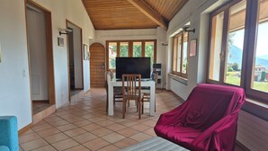 A room with a tiled floor, a wooden ceiling, a TV on a table, a covered chair, and a window with a view of greenery. - Executive Huge Flat in Central Lugano (Lugano)