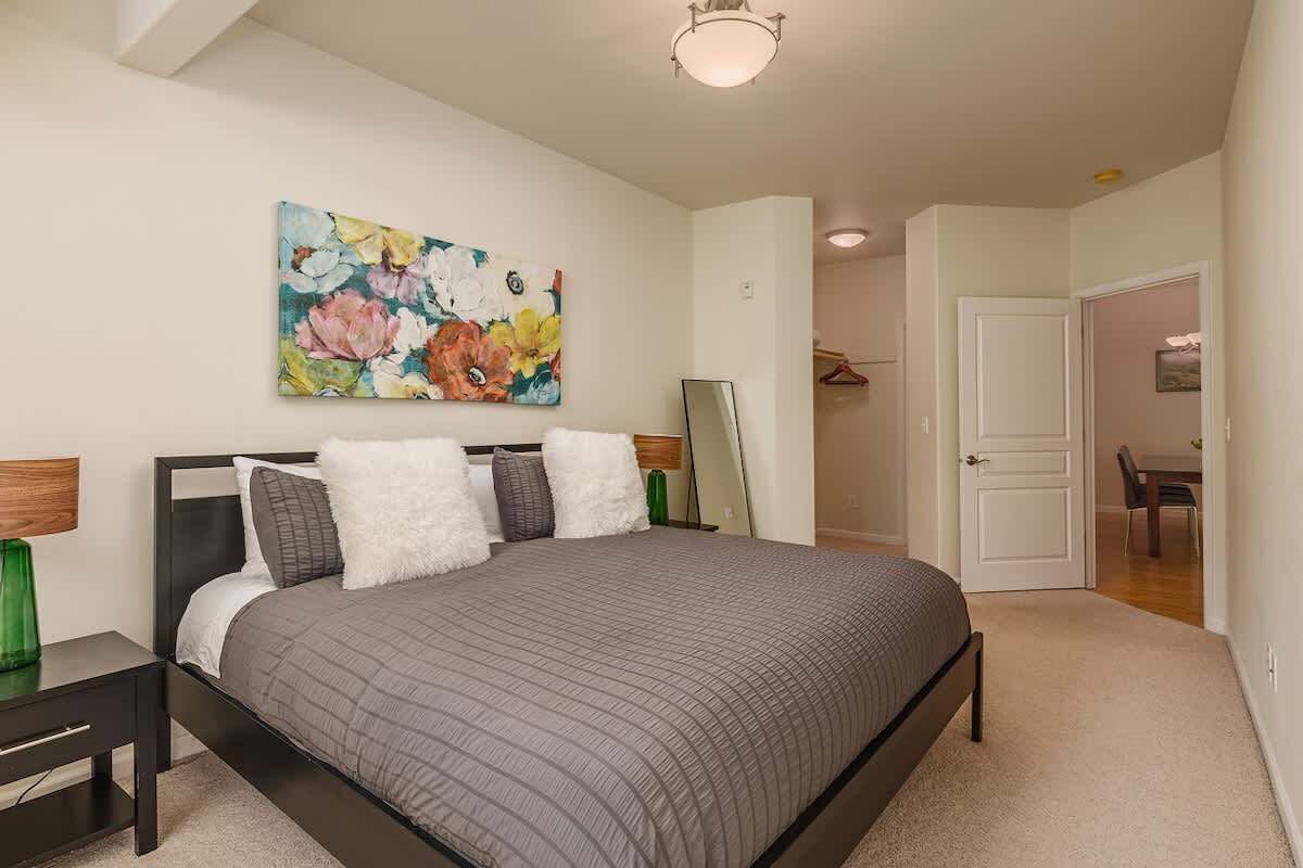 A bedroom with a bed, a painting, a mirror, and a door leading to another room.