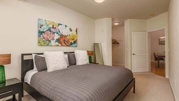 A bedroom with a bed, a painting, a mirror, and a door leading to another room.
