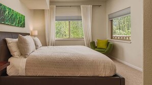 Een slaapkamer met een groot bed, een groene stoel en een raam met uitzicht op bomen.