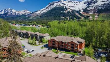 A multi-story building with a parking lot in front, surrounded by trees and mountains in the background.