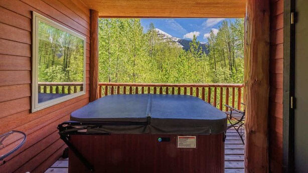 Een houten hutje met een jacuzzi op een terras, met uitzicht op een bos en bergen.