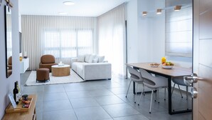 A modern living room with a sofa, chairs, a dining table, and a kitchen area with a breakfast setup. - SeaFront Luxurious  3BR Apartment | Mamad (Rishon LeTsiyon)