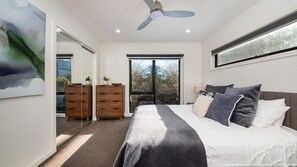 Une chambre moderne avec un grand lit, un ventilateur de plafond et une vue sur les arbres par la fenêtre.