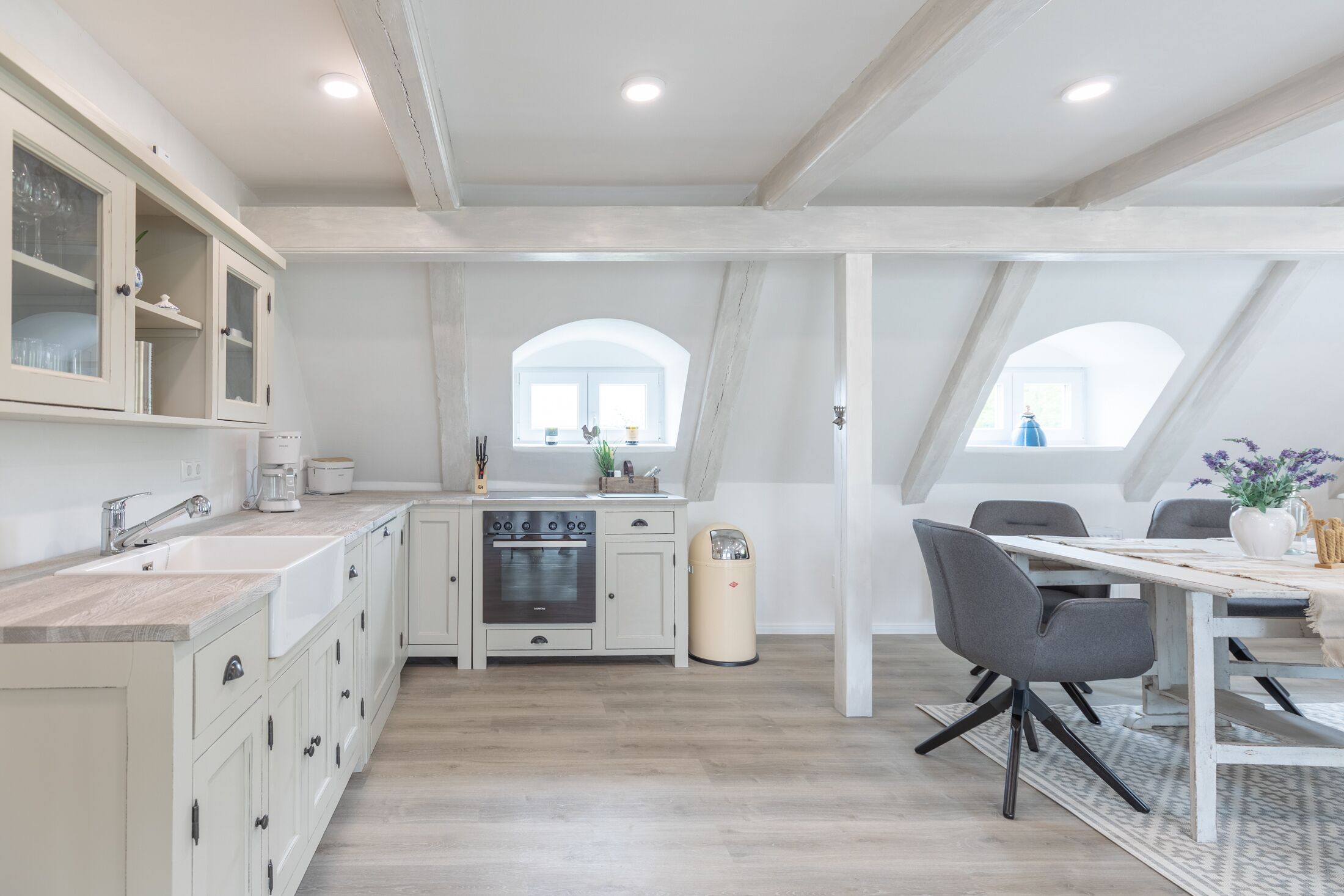 Una cocina moderna con armarios blancos, horno integrado y una zona de comedor con mesa y sillas.