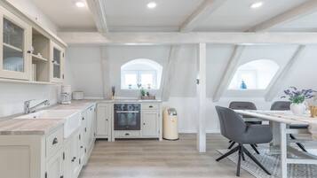 Una cocina moderna con armarios blancos, horno integrado y una zona de comedor con mesa y sillas.