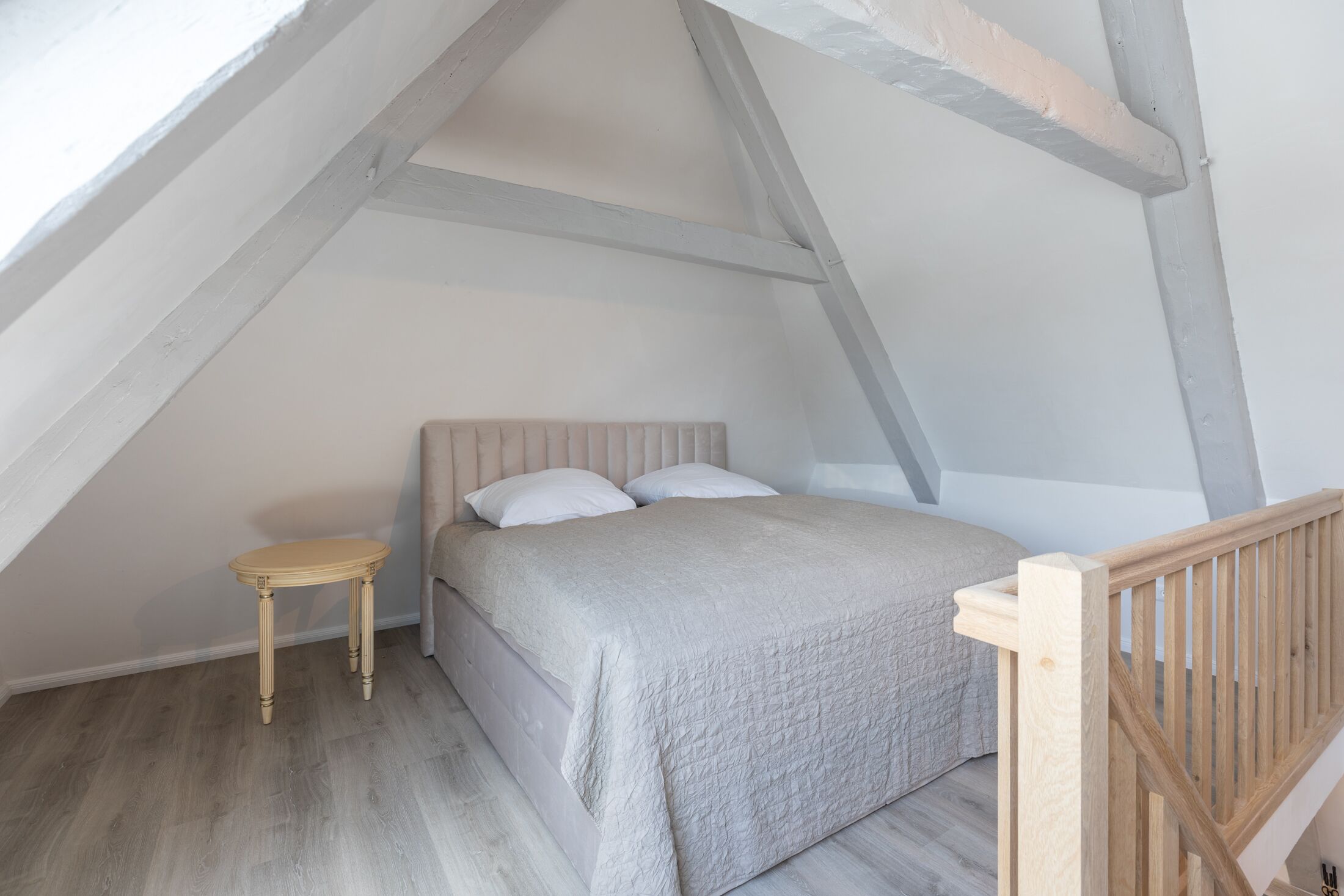 A bedroom with a bed, a small table, and a wooden railing.