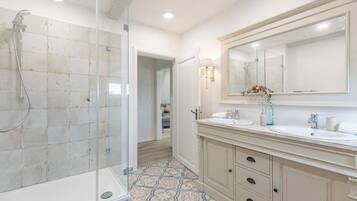 A modern bathroom with a glass-enclosed shower, two sinks, a large mirror, and patterned floor tiles.