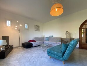 Uma sala de estar com sofá, mesa de centro, luminária de chão e luminária pendente.