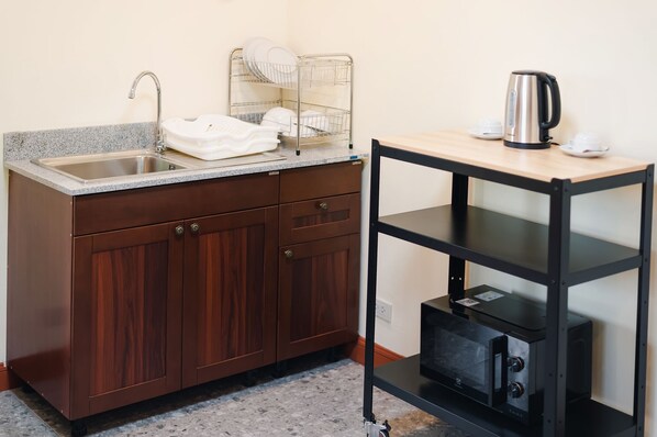 Una kitchenette con un lavamanos de acero inoxidable, un escurreplatos, una tetera y un microondas.
