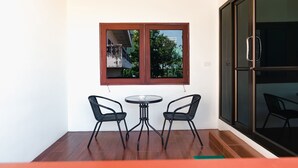 Ein kleiner Balkon mit Holzboden, ein Fenster mit Blick auf ein Gebäude und zwei schwarze Stühle um einen kleinen Tisch.