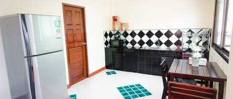 A compact kitchen with a refrigerator, a microwave, and a sink. There is a wooden door and a tiled backsplash.