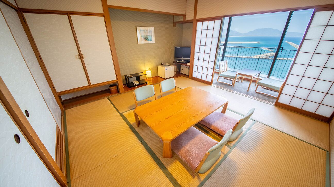 Une pièce de style japonais traditionnel, avec un sol recouvert de tatamis, une table en bois, des chaises, un téléviseur et un balcon offrant une vue.
