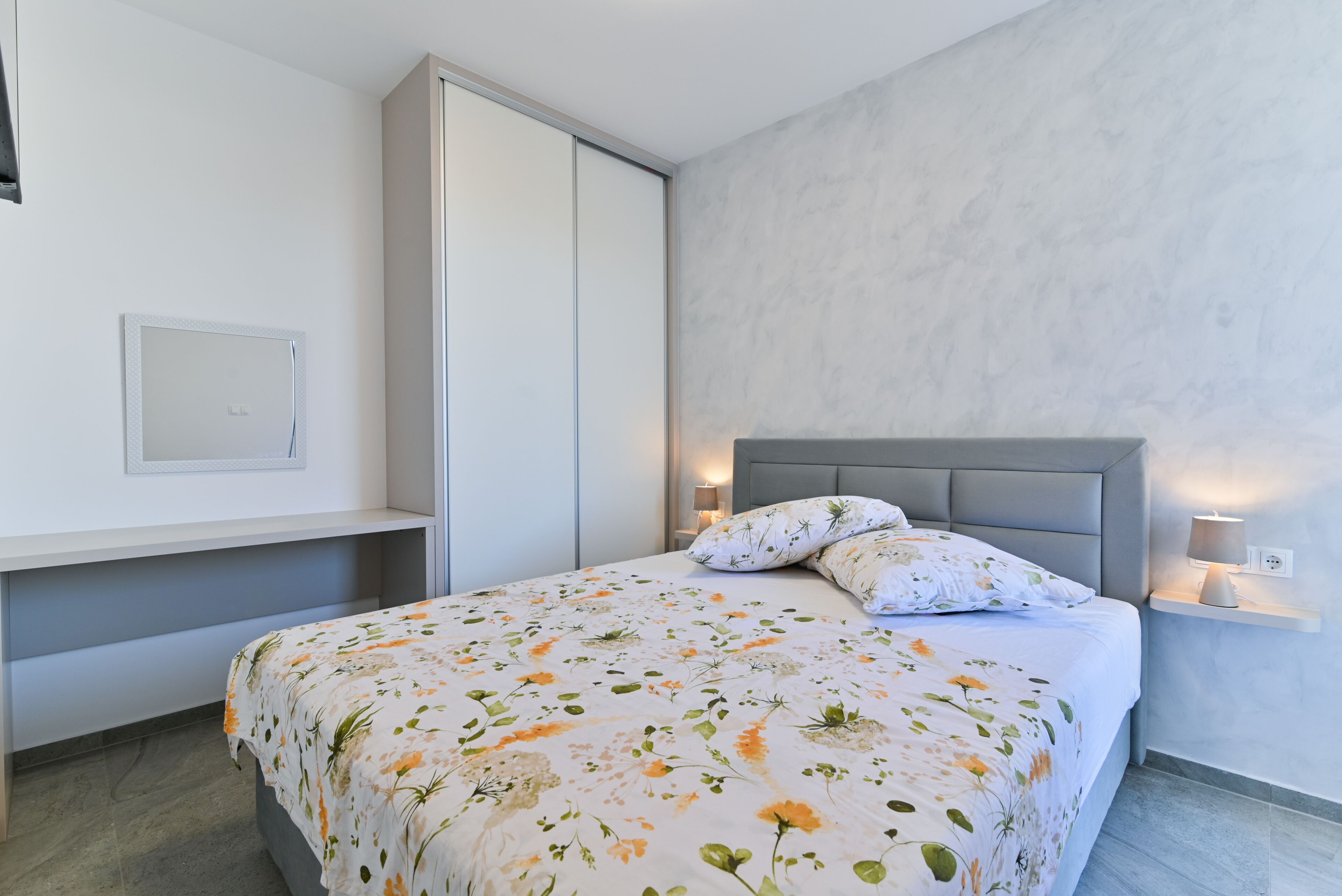 A modern bedroom with a bed, a nightstand, a wall-mounted TV, and a sliding closet door.