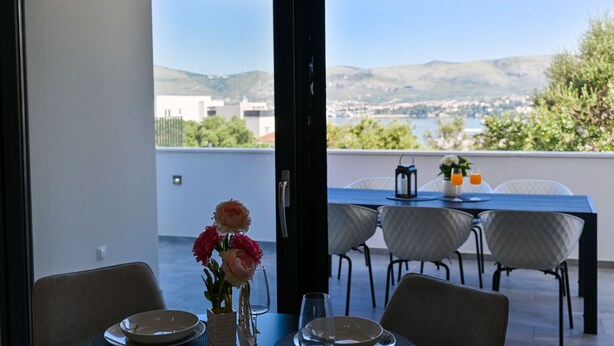 Un comedor con una mesa preparada para dos, un florero con flores y vistas a un lago y montañas.