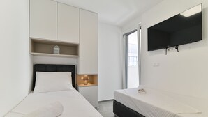 Habitación de hotel con cama, mesita de noche con lámpara, televisor montado en la pared y una ventana.