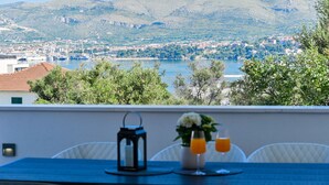 Una mesa con un farol, un jarrón con flores y dos vasos de zumo de naranja, con vistas a un pueblo costero y montañas al fondo.
