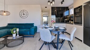 Una cocina moderna con electrodomésticos negros, un comedor con sillas grises y un sofá color turquesa.