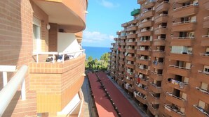 A multi-story residential building with balconies, a red pathway, and a view of the ocean.