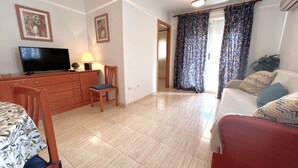 A living room with a television, a dining table with chairs, a sofa, and a window with curtains.