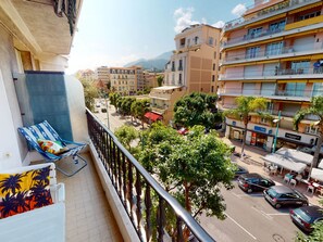 Un balcó amb una cadira blava i un coixí de colors, amb vista a un carrer ple de cotxes i edificis.