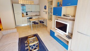 En kompakt opholdsstue med tekøkken, spiseplads og siddeområde med tv.