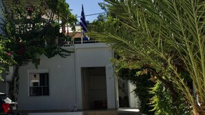 Een wit gebouw met een balkon, omringd door groen en een vlag.