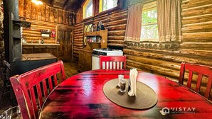 Ein rustikales Blockhaus-Interieur mit einem Holzesstisch, roten Stühlen, einer Küchenzeile mit Herd und einem großen Fenster.