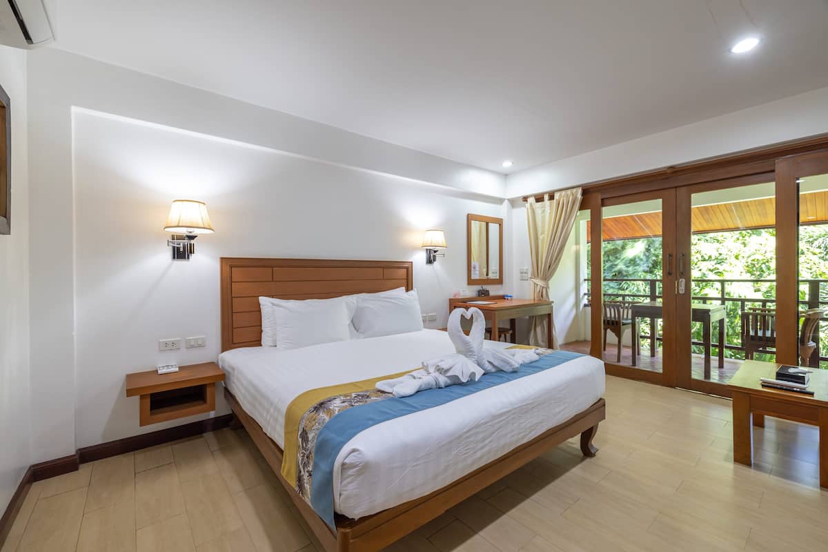 A hotel room with a wooden bed, two bedside tables, a desk, and a balcony with outdoor furniture.