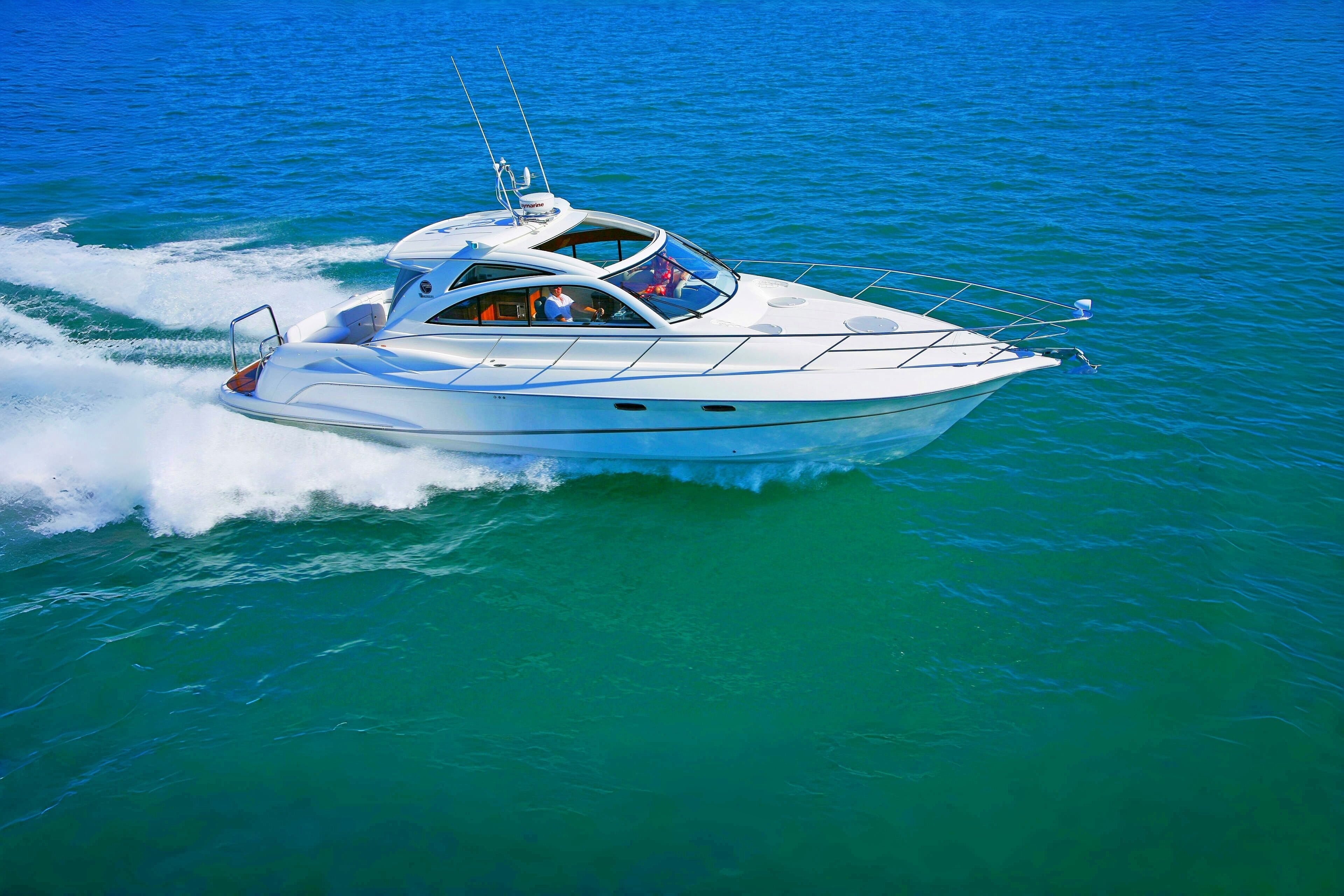 A white yacht with a covered deck and a cabin, moving through turquoise waters.