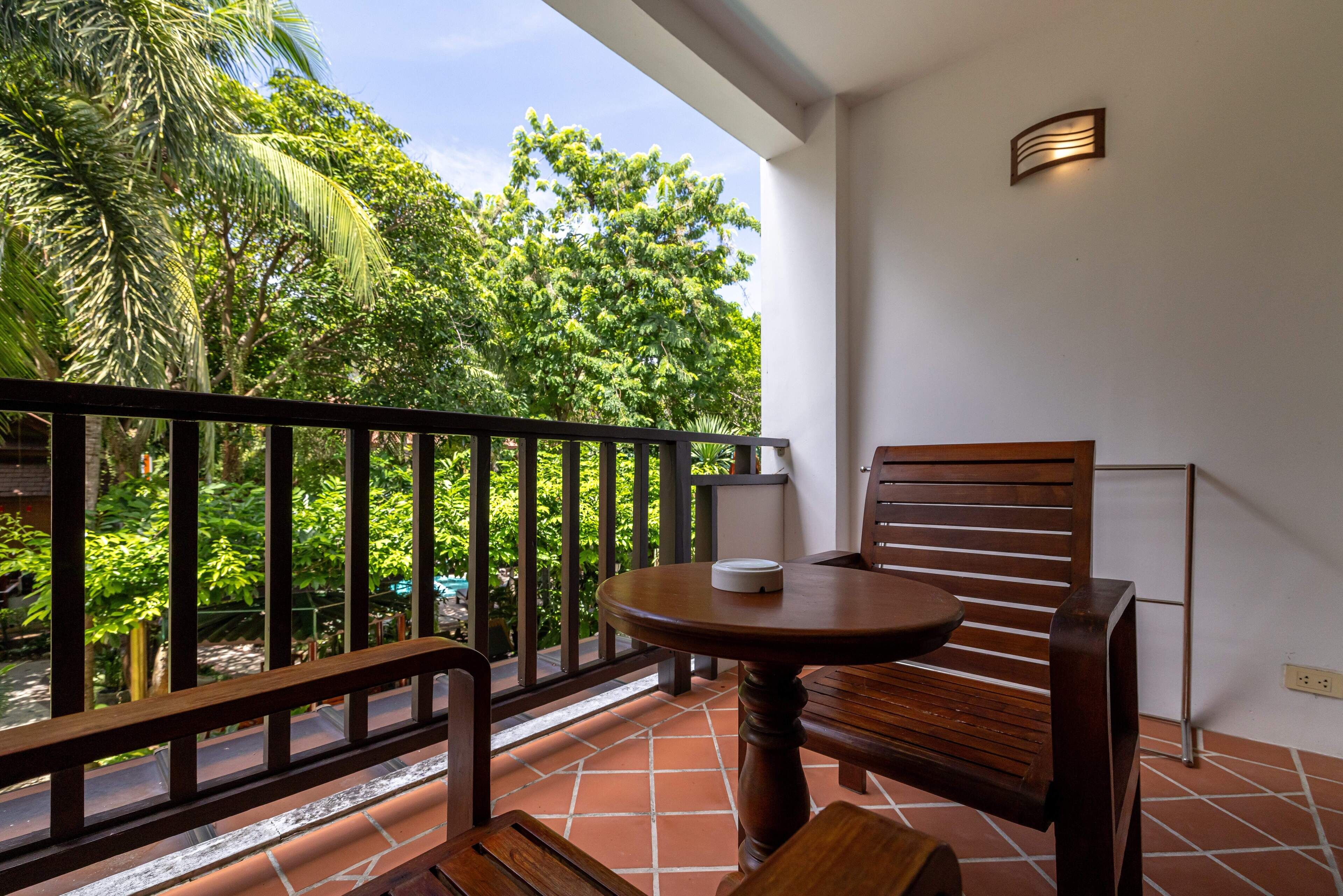 Un balcón con una silla y mesa de madera, baranda y vistas de vegetación exuberante.