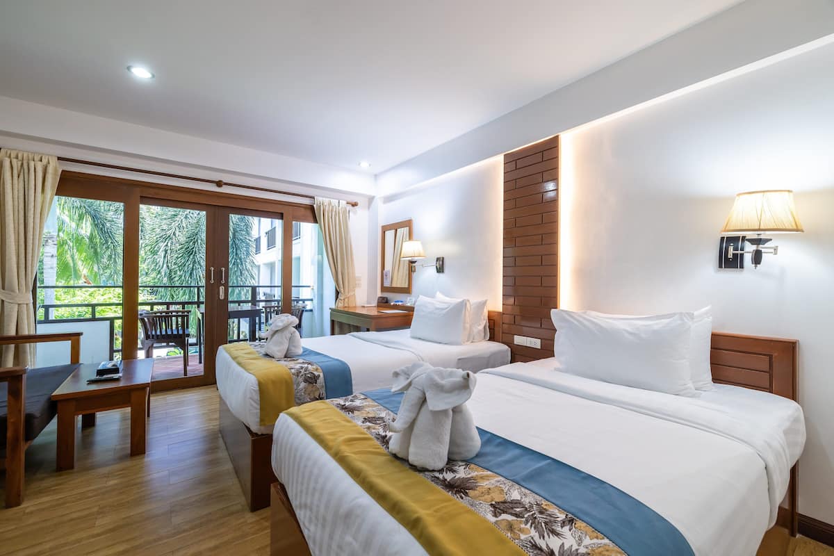 A hotel room with two beds, a desk, and a balcony.