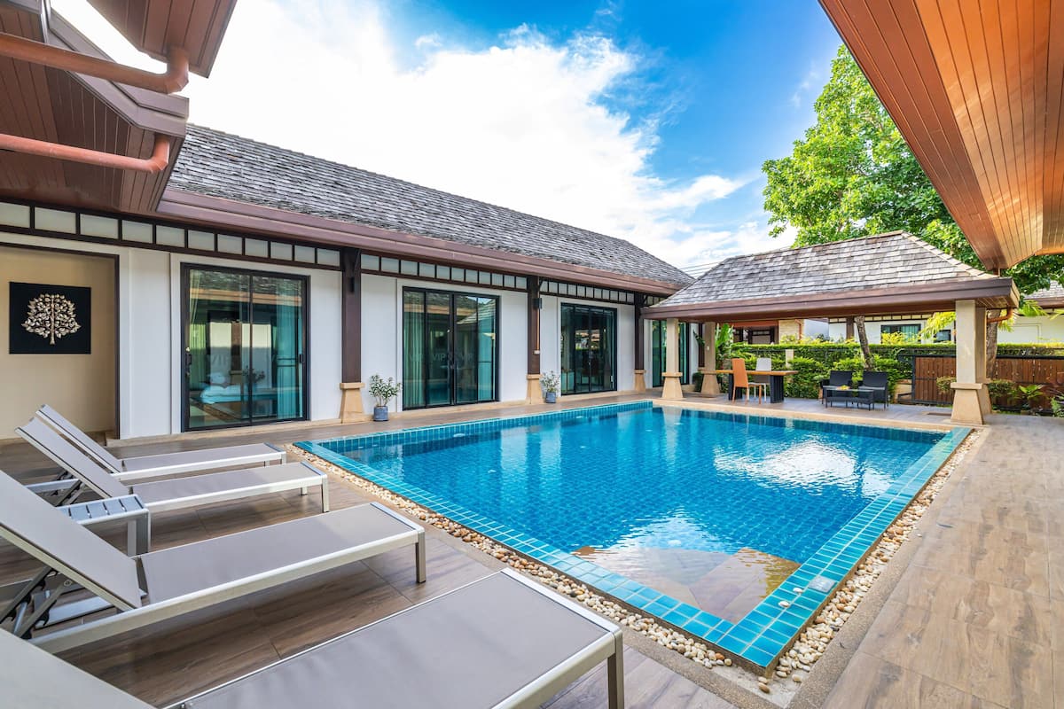 A swimming pool with lounge chairs, a covered patio, and a modern building with large windows.