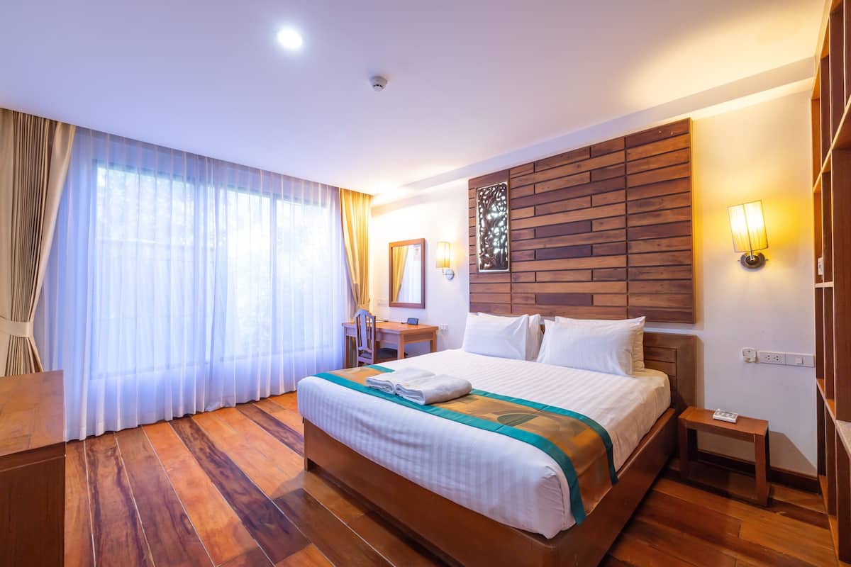 A hotel room with a wooden bed, a desk, a chair, and a large window with curtains.