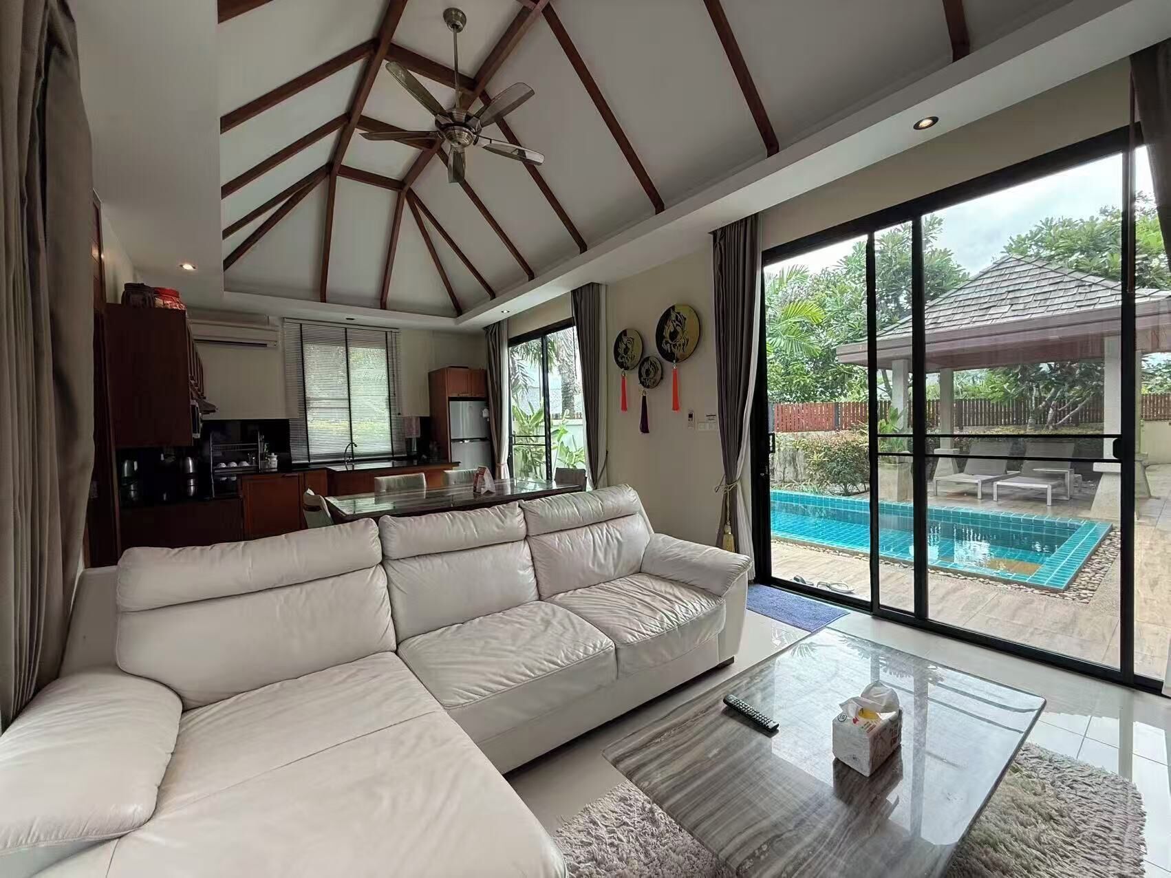 A spacious living area with a large white sofa, a glass coffee table, and a ceiling fan.