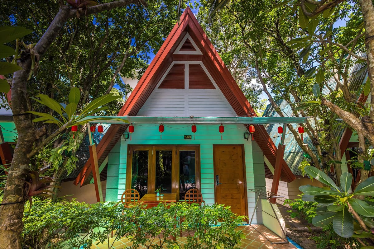 A traditional house with a red roof, wooden doors, and a porch with chairs.