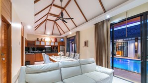 Un salon moderne avec un canapé blanc, un coin repas avec une table dressée pour quatre personnes et une vue sur une piscine.