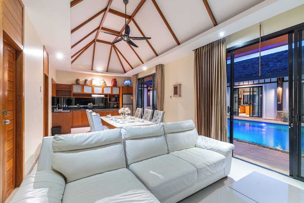 A modern living room with a white sofa, a dining area with a table set for four, and a view of a swimming pool.