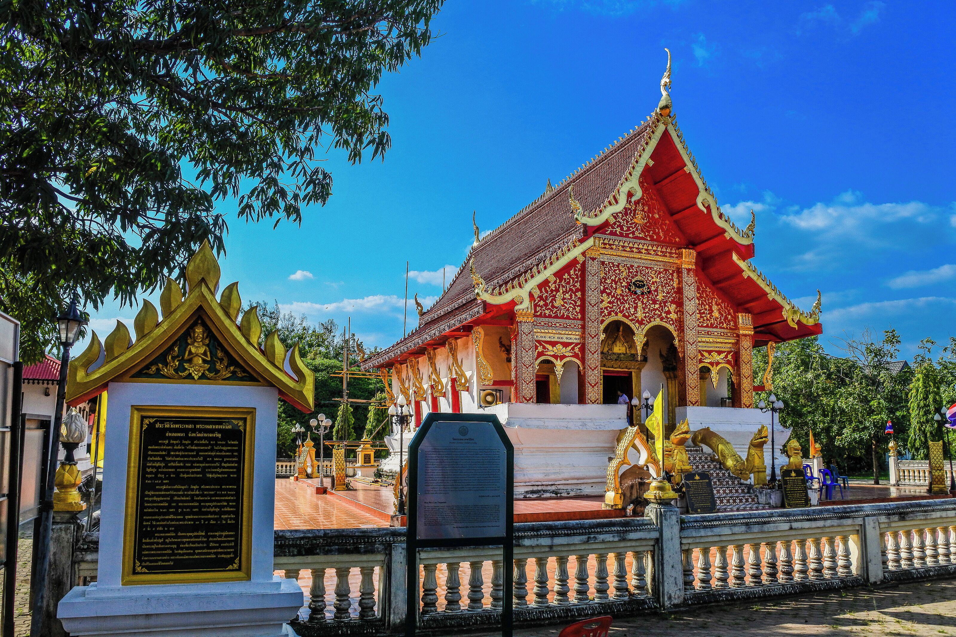 A traditional temple with a red roof and golden decorations, a white entrance, and a signboard in front.