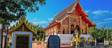 A traditional temple with a red roof and golden decorations, a white entrance, and a signboard in front.