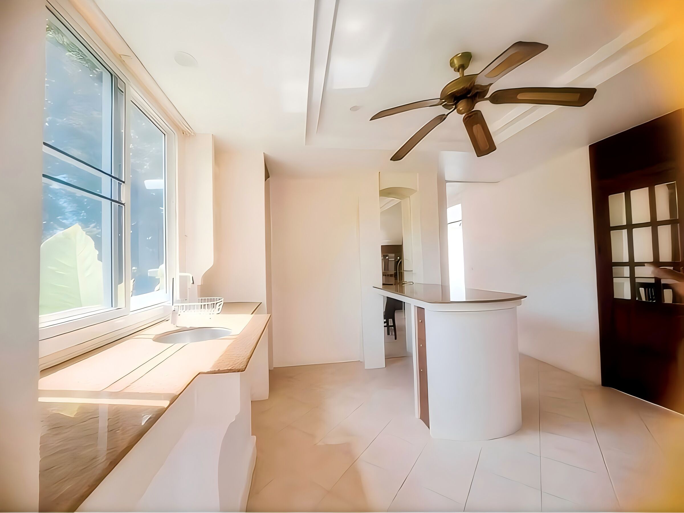 A modern bathroom with a large window, a ceiling fan, and a central sink area.