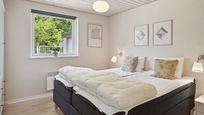 Ein Schlafzimmer mit Bett, einem Fenster mit Blick ins Grüne und Wandbildern.