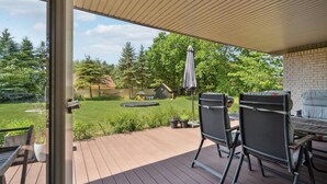 Eine überdachte Terrasse mit Blick auf einen Garten, inklusive Trampolin und Spielhaus.