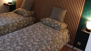 Ein Zimmer mit zwei Betten, jeweils mit gemusterten Bettbezügen, einem Holzschrankgitter-Kopfstück und Nachttischlampen.
