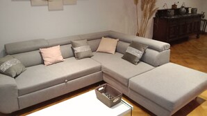 Ein graues Ecksofa mit vielen Kissen, ein weißer Couchtisch und eine dekorative Wandgestaltung.