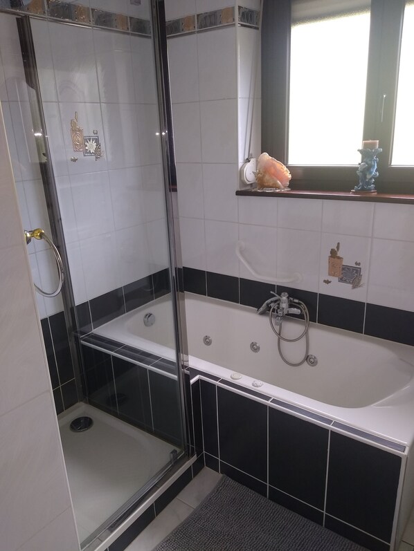 Un baño con ducha envuelta en vidrio, bañera y ventana con estante decorativo.