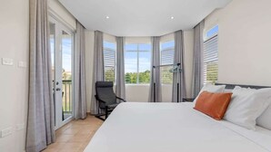 A bedroom with a large bed, a chair, and a balcony with curtains. - Moonlight Villa | Harbour Lakes at Palmas del Mar (Palmas Del Mar)