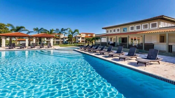 A swimming pool with lounge chairs and a building with a tiled roof. - Moonlight Villa | Harbour Lakes at Palmas del Mar (Palmas Del Mar)